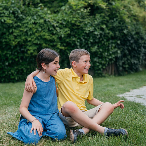 girl and boy sitting on the grass side by side and laughing
